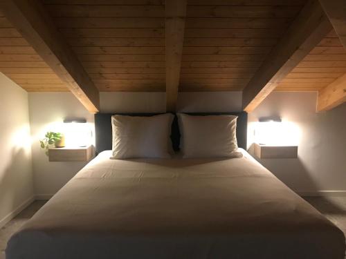 a bed with two pillows in a room with two lights at Sotto La Vigna Charm Stay Adults only vacation Appartement Hayloft in Montegrosso dʼAsti