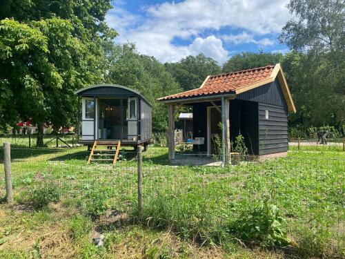 a small shed in a field with a house at Tiny house, pipowagen onder de kastanje in Aalten