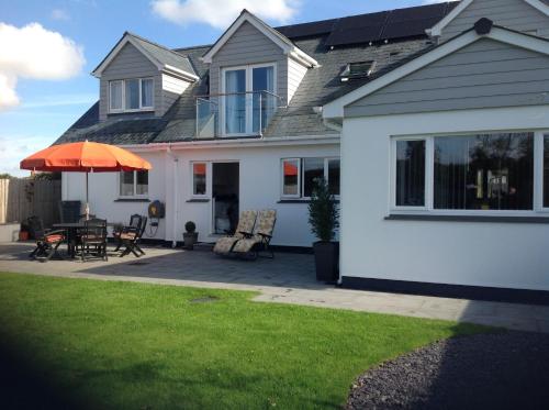 Cette maison blanche dispose d'une terrasse avec un parasol orange. dans l'établissement Hedlea, à Redruth