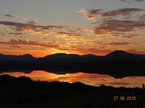 a sunset with a reflection of mountains in the water at Cill Cottage in Roundstone