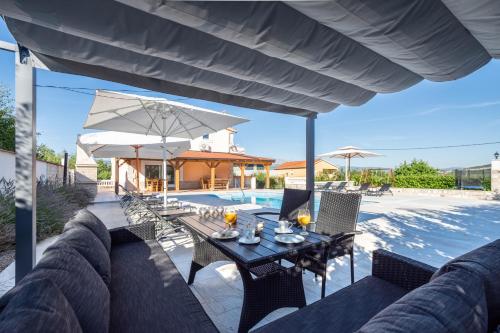 um pátio com uma mesa, cadeiras e um guarda-sol em Vacation villa Matic with 7 bedrooms em Sinj
