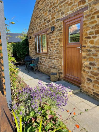 Warmington的住宿－Honeysuckle Cottage - Hillside Holiday Cottages, Cotswolds，砖屋,木门和紫色的鲜花