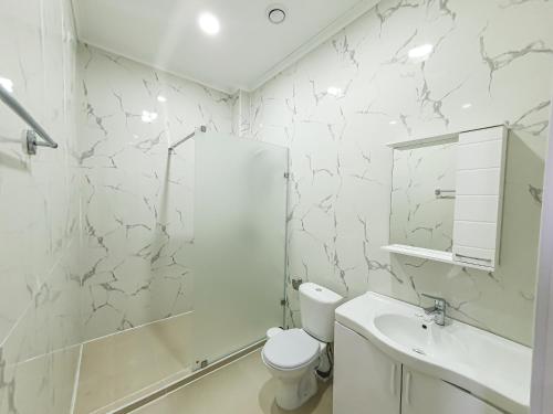 a white bathroom with a toilet and a sink at Ritz Hotel in Atyrau
