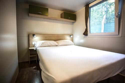 Campeggio Al Bosco في غرادو: سرير أبيض كبير في غرفة مع نافذة
