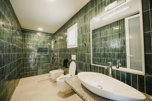 Baño de azulejos verdes con lavabo y aseo en Drymades Bungalows Adults Only, en Dhërmi