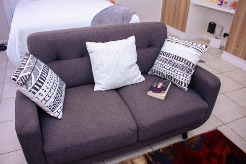 a couch with pillows and a book on it at Charms and bows studio apartment -near ORT airport in Boksburg