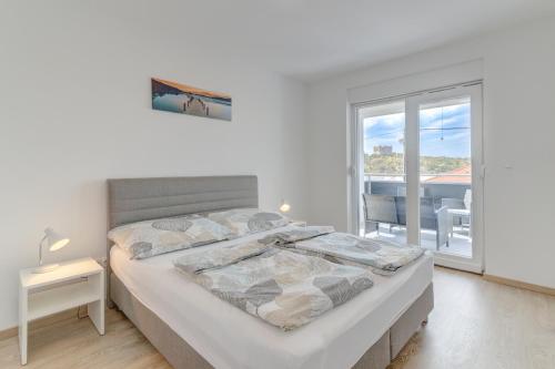 a white bedroom with a large bed and a window at Damar Apartmani in Senj