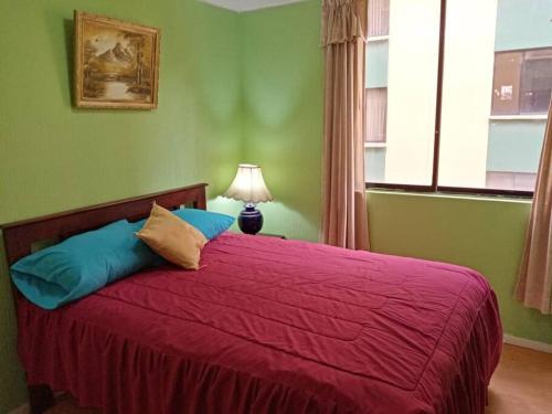1 dormitorio con 1 cama con edredón rojo y ventana en Hermoso Apartamento al Norte cerca de la Embajada Americana, en Quito