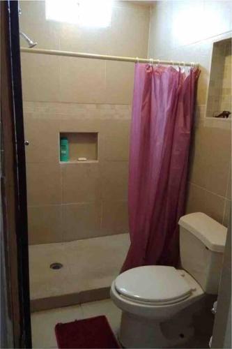 a bathroom with a toilet and a pink shower curtain at Capistrano Suites in Hermosillo