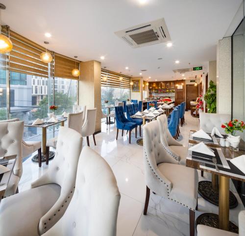 un restaurante con sillas blancas, mesas y ventanas en Menora Premium Da Nang - Sea Corner Boutique, en Da Nang