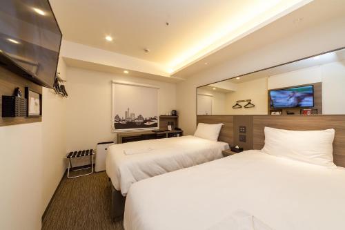 a hotel room with two beds and a flat screen tv at Smile Hotel Hiroshima in Hiroshima
