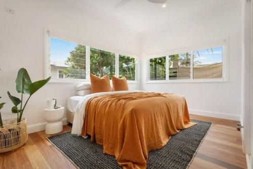 a white bedroom with a bed with an orange blanket at Fuller Holidays - Hacienda, Luxury 5 bedroom home with pool in Byron Bay
