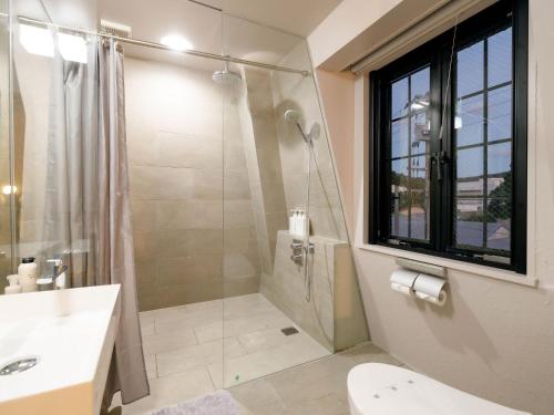 a bathroom with a shower and a toilet and a sink at Denpaku Amami Hotel in Amami