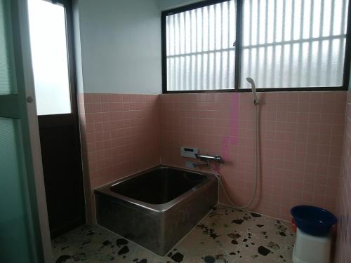 y baño alicatado de color rosa con bañera y ventana. en みのる民泊1号, en Shibushi