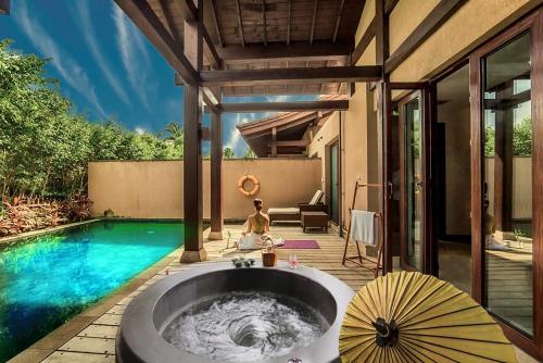 a woman sitting in a bath tub next to a swimming pool at Narada Resort & Spa Perfume Bay Sanya - All Villas in Lingshui
