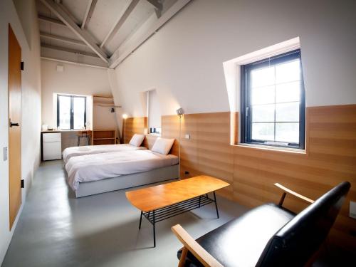 ein Schlafzimmer mit einem Bett, einem Tisch und einem Stuhl in der Unterkunft Denpaku Amami Hotel in Amami