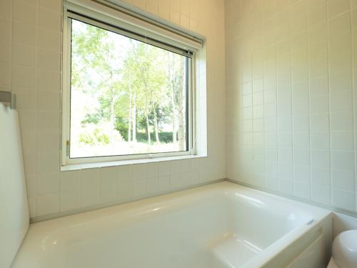 La salle de bains blanche est pourvue d'une baignoire et d'une fenêtre. dans l'établissement Coboushi オモヤ, à Niseko