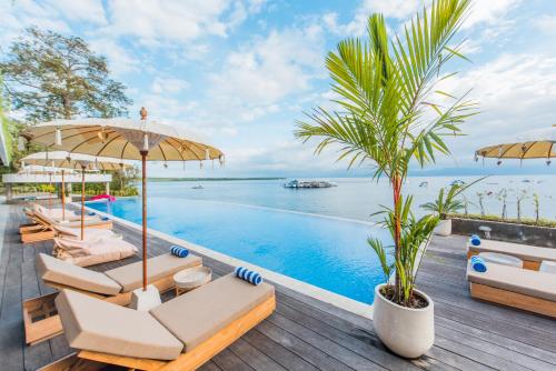 ペニダ島にあるSea La Vie Resort Nusa Penidaのリゾートのインフィニティプール(椅子、パラソル付)