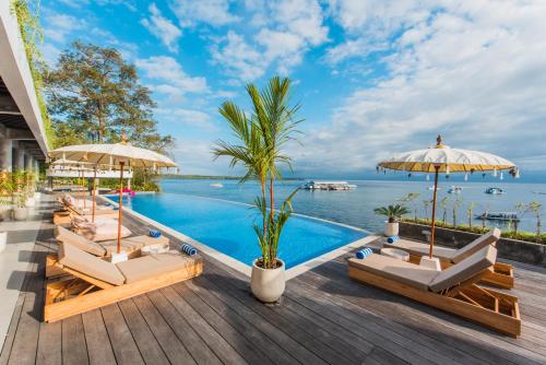 a pool with chairs and umbrellas on a deck at Sea La Vie Resort Nusa Penida in Nusa Penida