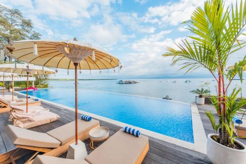a pool with chairs and an umbrella and the ocean at Sea La Vie Resort Nusa Penida in Nusa Penida