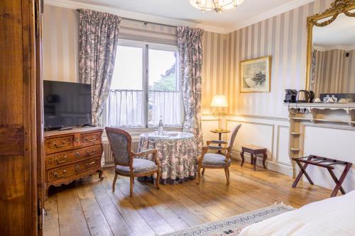 ein Hotelzimmer mit einem TV und einem Tisch mit Stühlen in der Unterkunft Le Manoir des Impressionnistes - Bord de Mer in Honfleur