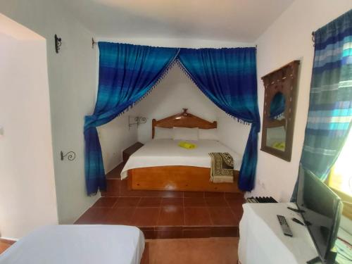 um quarto com uma cama com cortinas azuis e uma televisão em Dar layla moulati em Chefchaouen