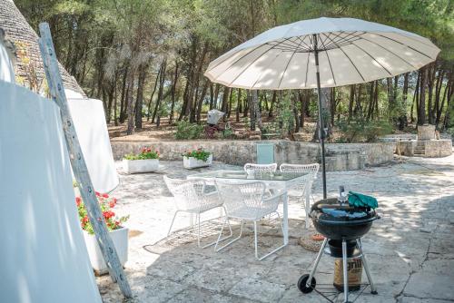 - une terrasse avec une table, un parasol et un grill dans l'établissement Trulli del 1800 con Foresta, Wi-Fi e Biciclette, à Cisternino