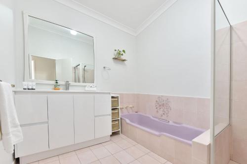 La salle de bains est pourvue d'une baignoire pourpre et d'un miroir. dans l'établissement Sunshine Shores, à Morisset East