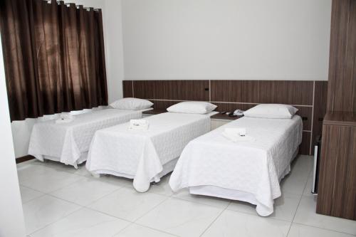 a room with three beds with white sheets at Miotto Executive Hotel in Navegantes