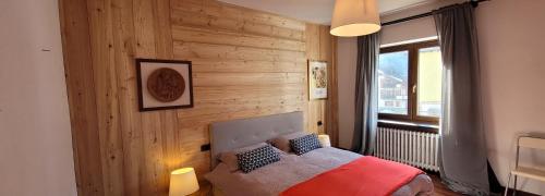 1 dormitorio con pared de madera, cama y ventana en Appartamento Adalpina, en Santo Stefano di Cadore