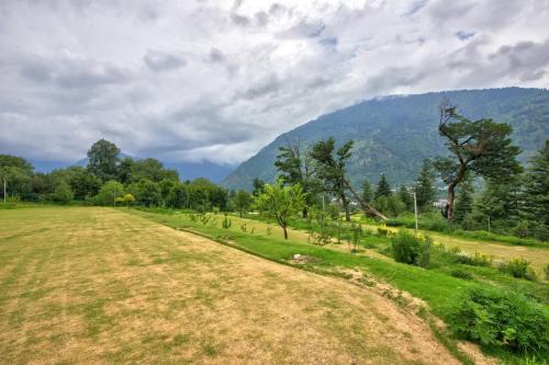 a field with trees and mountains in the background at Anand Vardhan Resorts in Manāli