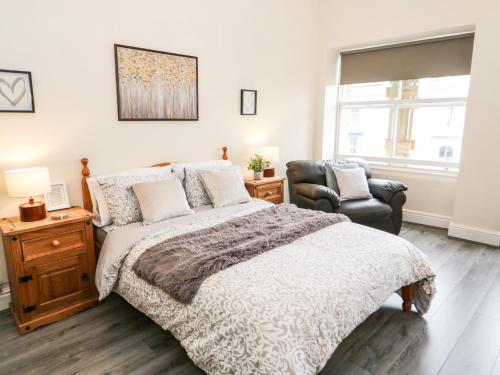 um quarto com uma cama, uma cadeira e uma janela em Gerrard House Apartment em Llandudno