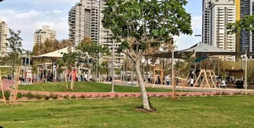a park with a tree and a playground and buildings at Hotel Apartment Short Term Tel Aviv Bat Yam 5 in Bat Yam