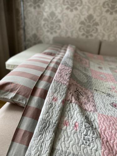 a bed with a pink and white quilt on it at Venta apartament in Mažeikiai