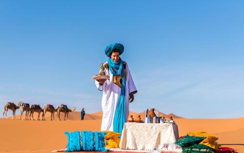 Un hombre en el desierto con una mesa y camellos. en The Desert Palace, en Merzouga