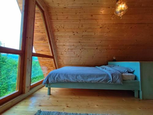 a bed in a wooden room with a large window at La sat - Blândă Mărie in Bertea