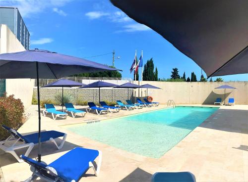 a swimming pool with blue chairs and umbrellas at Holiday Inn Express Montpellier - Odysseum, an IHG Hotel in Montpellier