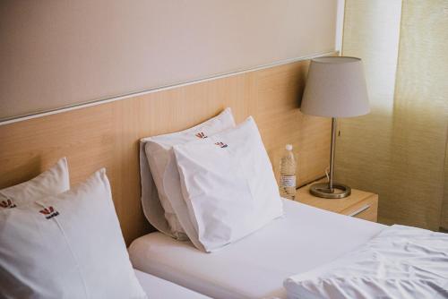 Una cama con almohadas blancas y una botella de agua. en Wabi Hotel - Beauty & Dental Center en Sopron
