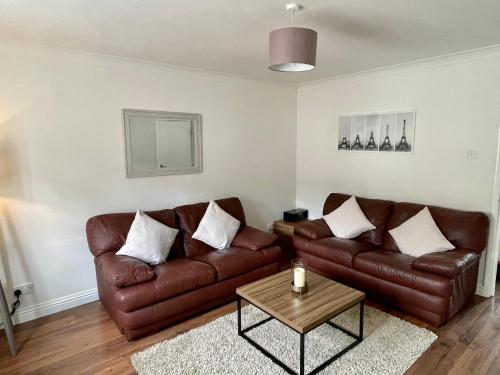 a living room with a brown leather couch and a table at Modern 2 bedroom apartment near Glasgow Airport in Paisley