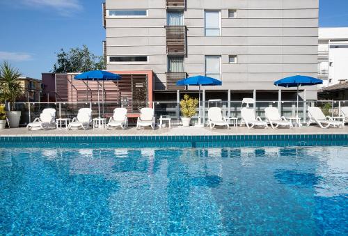 a swimming pool with chairs and umbrellas and a building at Hotel Rosanna 3 Stelle Superior in Lido di Jesolo