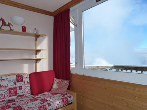 Cette chambre dispose d'un fauteuil rouge et d'une grande fenêtre. dans l'établissement Studio chaleureux au pied des pistes avec balcon - FR-1-181-2590, à Aime La Plagne