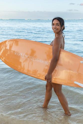 a woman walking on the beach holding a surfboard at VIVE Hotel Waikiki in Honolulu
