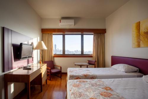 Cette chambre comprend deux lits, un bureau et une télévision. dans l'établissement Hotel Nacional Inn Belo Horizonte, à Belo Horizonte