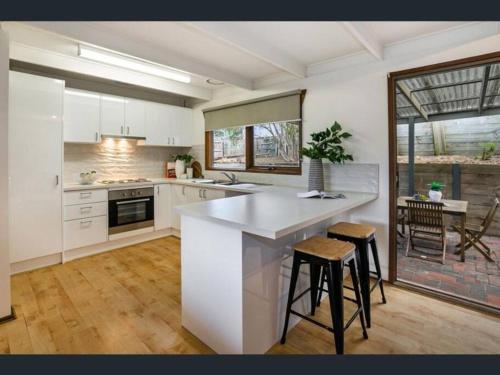 a kitchen with a large white counter and stools at Modern Beach House -Large Entertainers Deck ,Wineries, Hot Springs and Golf in Rye