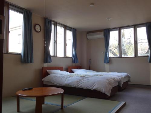a bedroom with a bed and a table and windows at Oomukou Ryokan in Hakuba