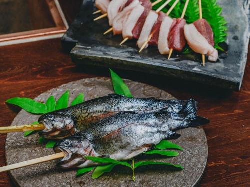 a table with two fish and meat on skewers at Kominkayado LOOF Kyonoie in Ōwatari