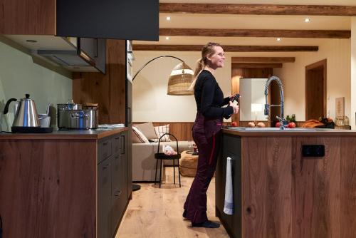 a woman standing in a kitchen drinking from a sink at Berghaus Schröcken - Hotel Apartments Spa in Schröcken