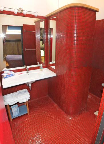 La salle de bains est pourvue de carrelage rouge, d'un lavabo et d'un miroir. dans l'établissement Les Cornadis, à Saint-Priest-sous-Aixe