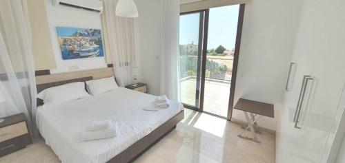 a white bedroom with a bed and a balcony at St. Georgiana Villa 7 in Peyia