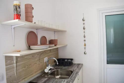 uma cozinha com um lavatório e um balcão com pratos nas prateleiras em Troi beach house em Vlorë